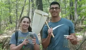 Two Ferrum students standing in a wooded area. One of them holds a small net.