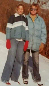 Jim Chidester '80 and Trish Mays '80 in college, standing with blue winter clothes on and red mittens, on a snowy hill