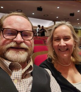 Jim and Trish Chidester '80 selfie in a theatre with red seats behind them.