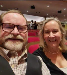 Jim and Trish Chidester '80 selfie in a theatre with red seats behind them. 