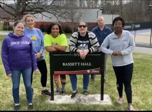 Members of the Office of Student Life & Engagement stand near the Bassett Hall sign, the building housing their offices.