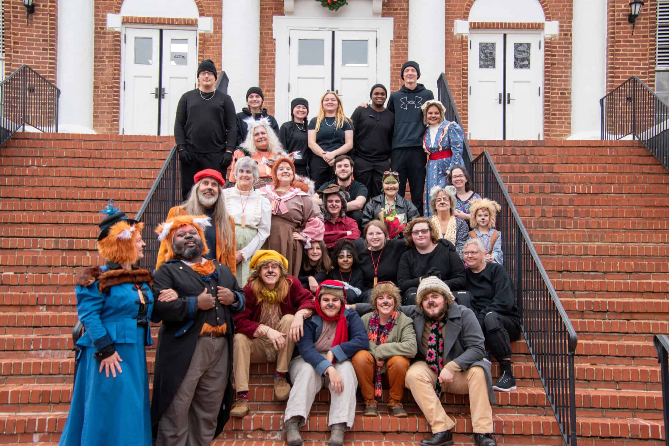 Emmet Otter 2023 cast on brick steps of Schoolfield Hall, child and adult actors in animal costumes, with crew members and some puppeteers in black