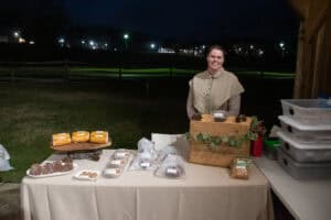 Vendor in brown dress at a table of baked goods at BRIM Christmas event outdoors