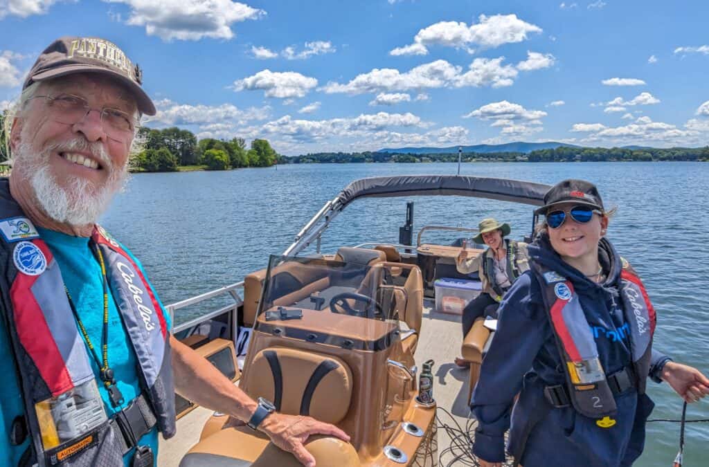 Three adults on a motorboat with tan seats, with blue lake water and blue sky and fluffy clouds
