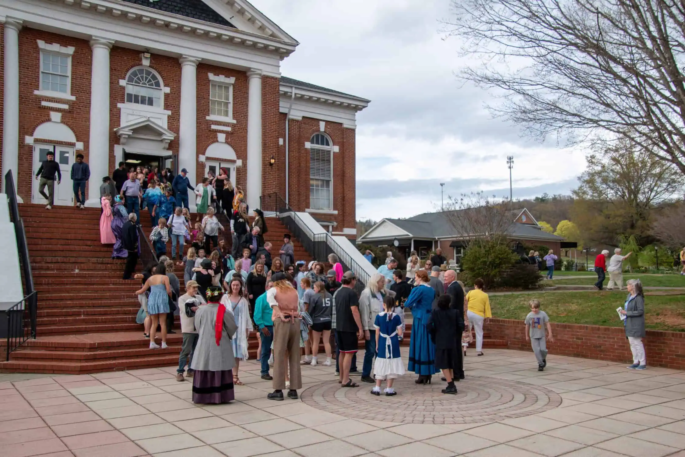 Crowd of audience members and Mary Poppins cast in costumes on steps of red brick theatre in Schoolfield Hall on campus