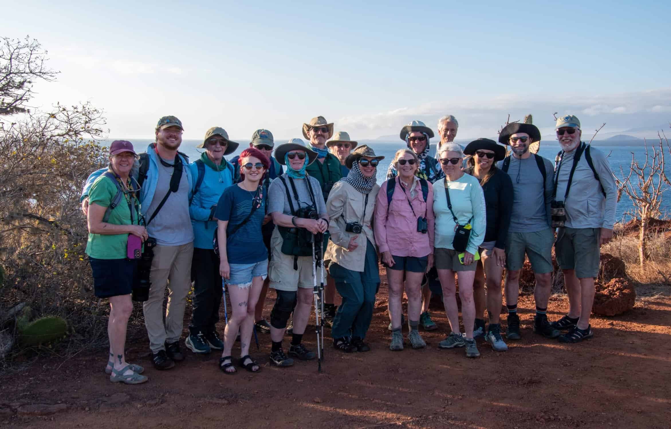 Group of adults in warm-weather travel clothes with bits of Galapagos landscape in background.