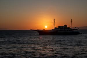 Deep orange Galapagos sunset with bright sun near horizon over one end of a long boat