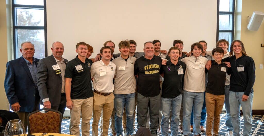 Billy Wagner with two rows of young men in baseball team and current and former coach at alumni awards ceremony in front of a blank screen and windows