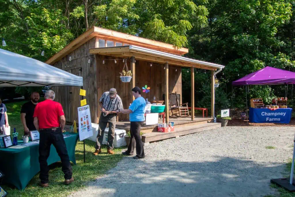 Wooden shed at Ferrum Park behind gravel drive with several market-goers in foreground