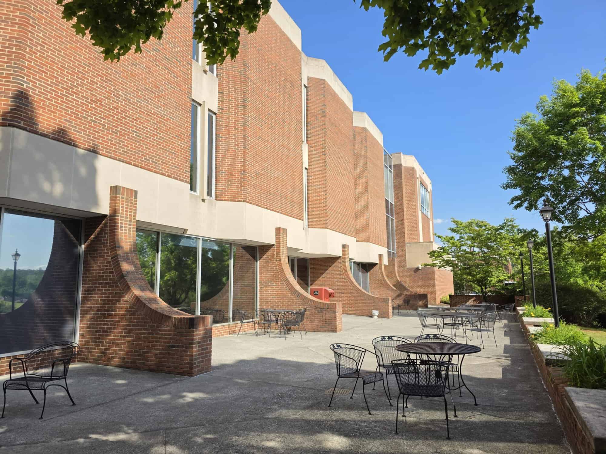 Back of Stanley Library with brick and concrete walls, curved modern brick buttresses at bottom, patio with black table and chairs