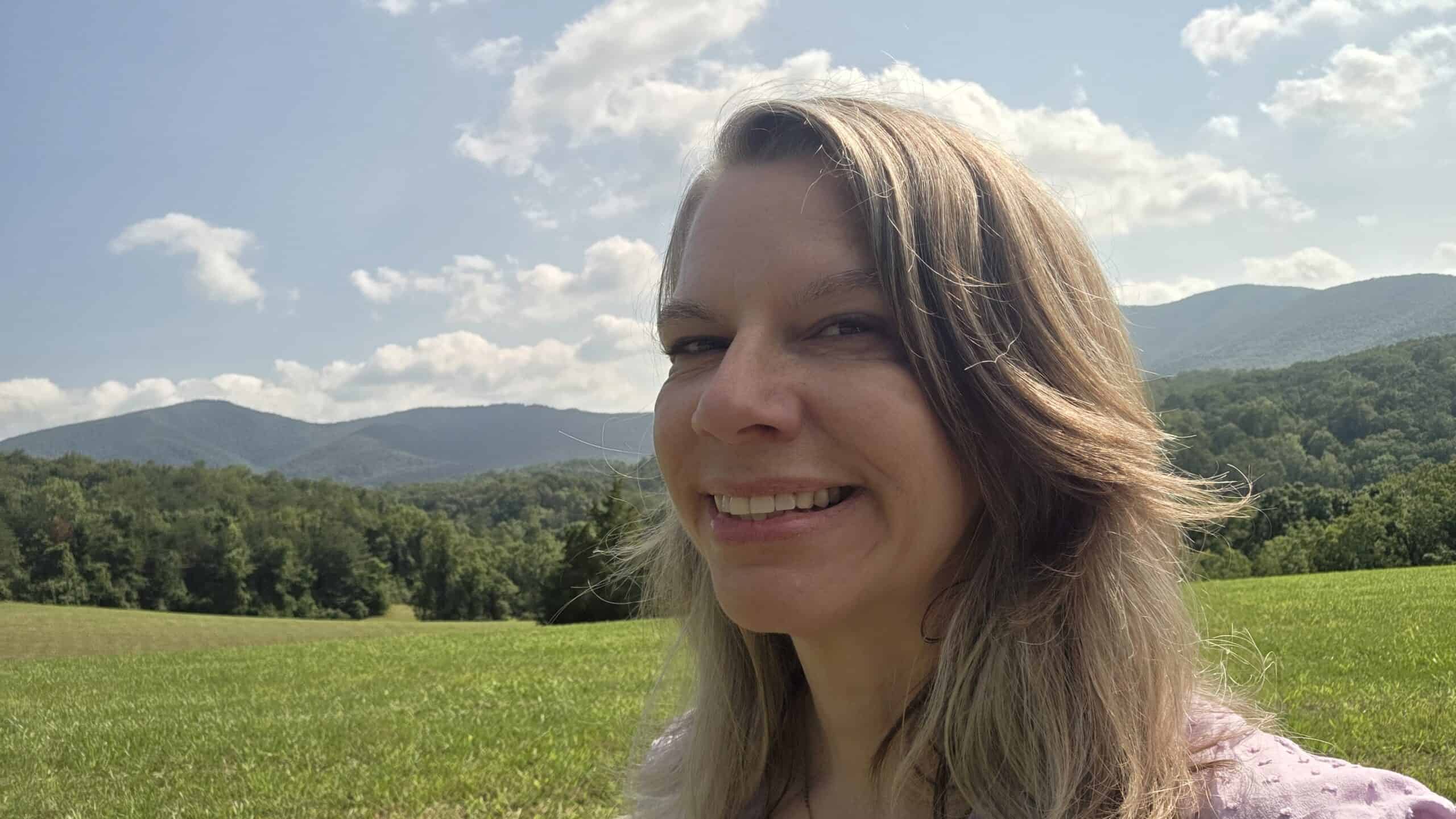 Headshot of woman facing left with long light hair, hills and grass in background