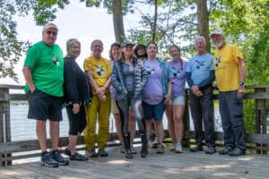 Ten students and adults in summer clothes lined up with trees behind them