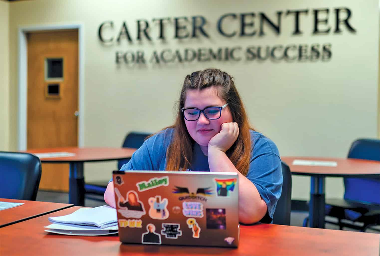 A student with an open laptop in front of her with the Carter Center sign behind her