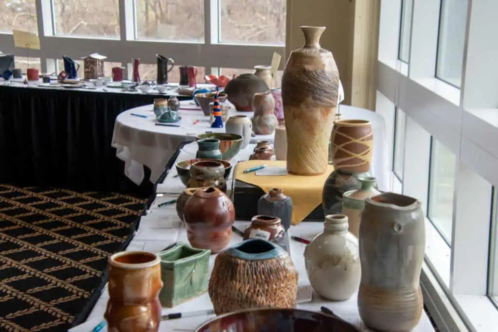 Silent auction at Empty Bowls, with many ceramic items on long tables in front of windows