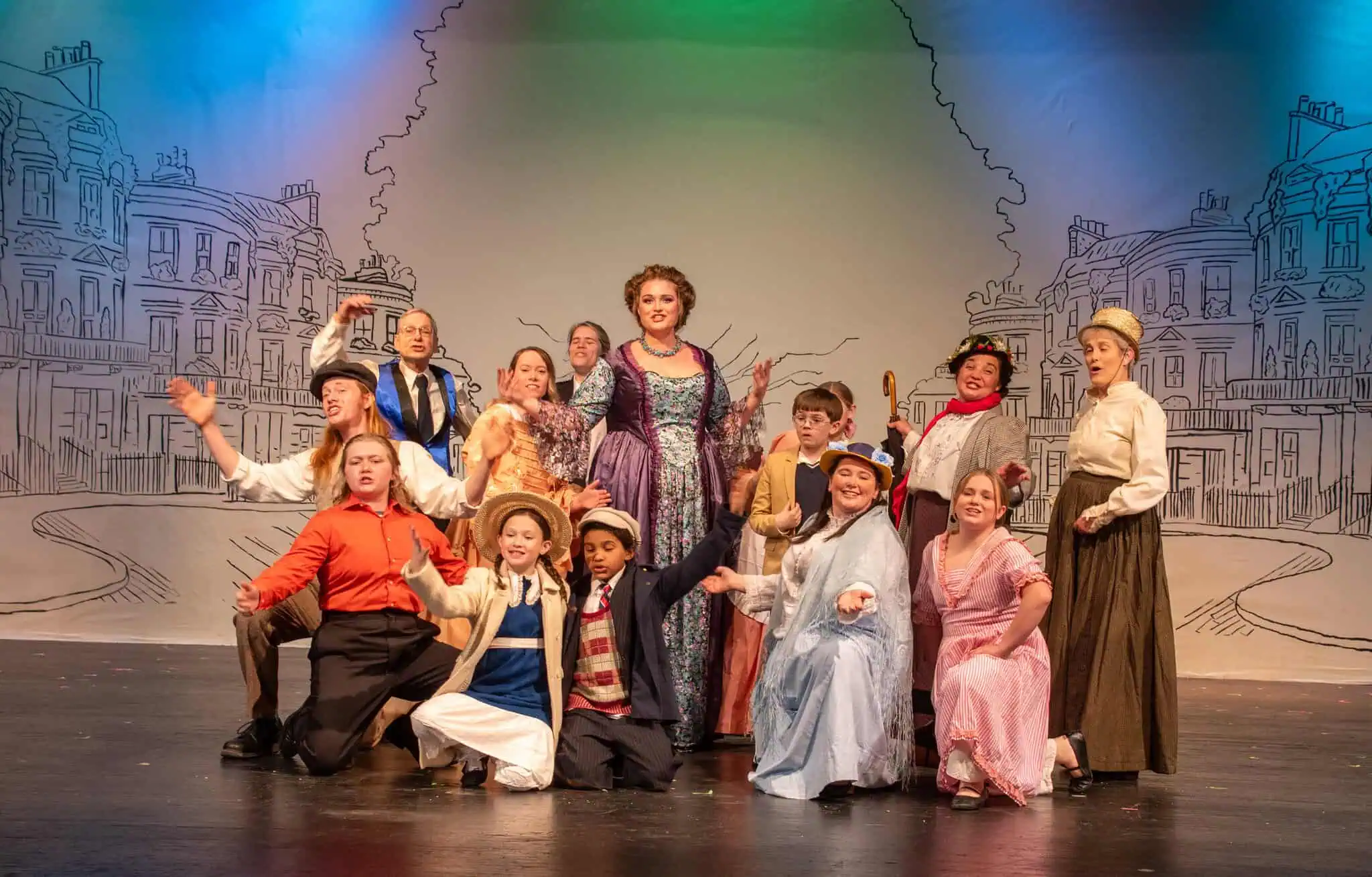 Scene from "Mary Poppins" with more than a dozen cast members in colorful costumes posing on stage, some with outstretched arms and some kneeling