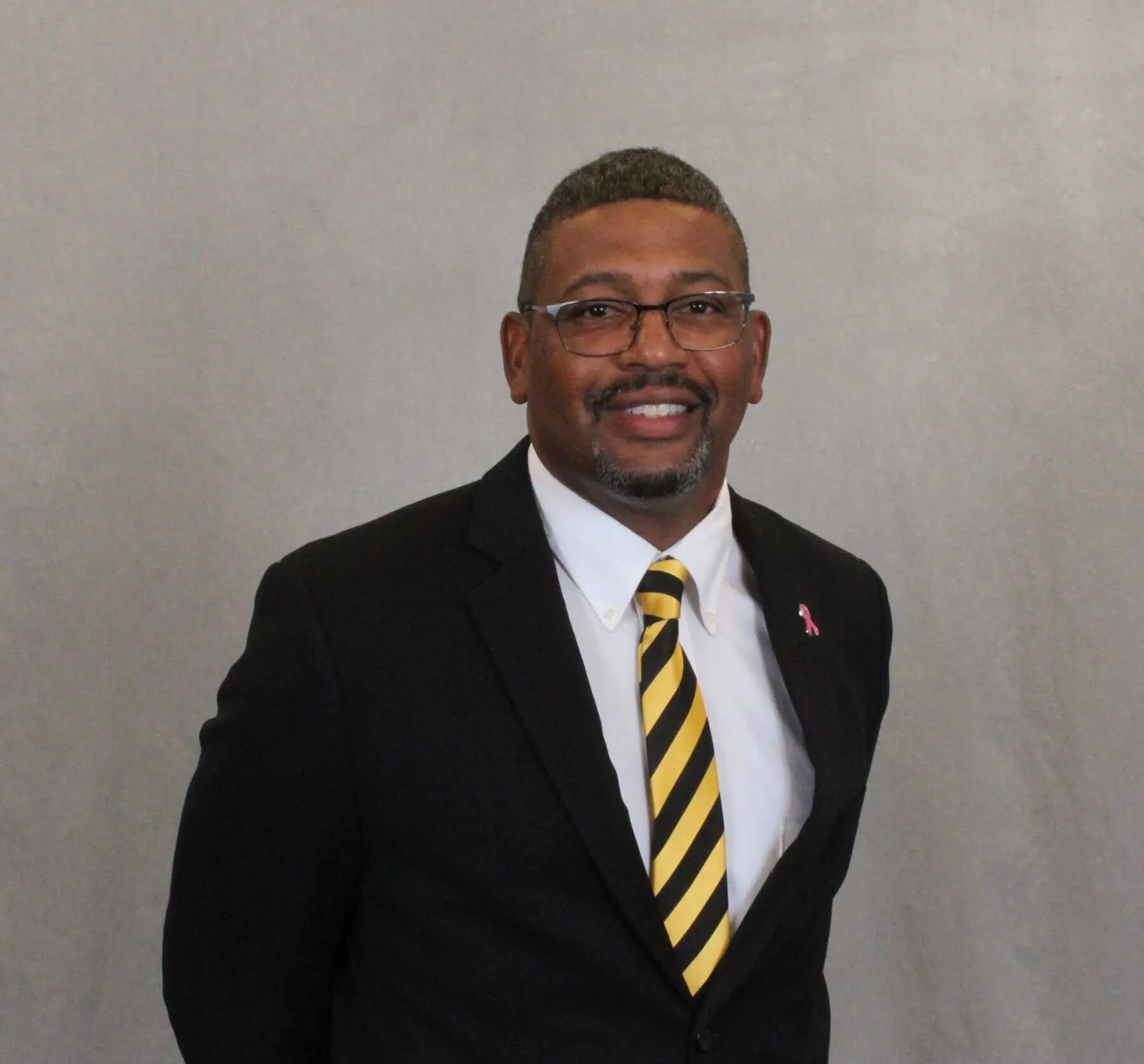 Head shot of Cleive Adams with glasses and short hair, dark jacket, white shirt, and tie with black and gold stripes