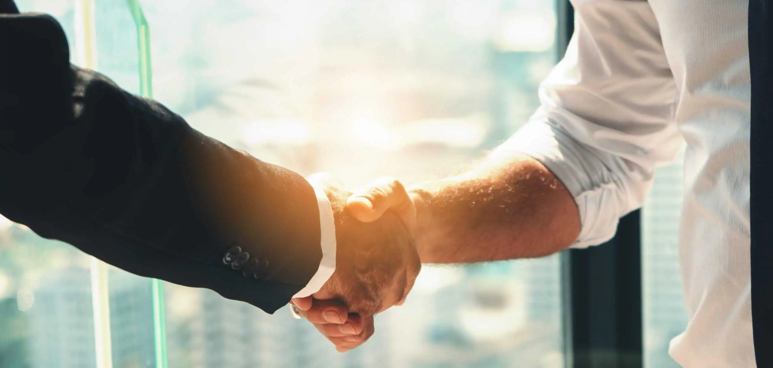 close up of two men's arms shaking hands in front of a glass window