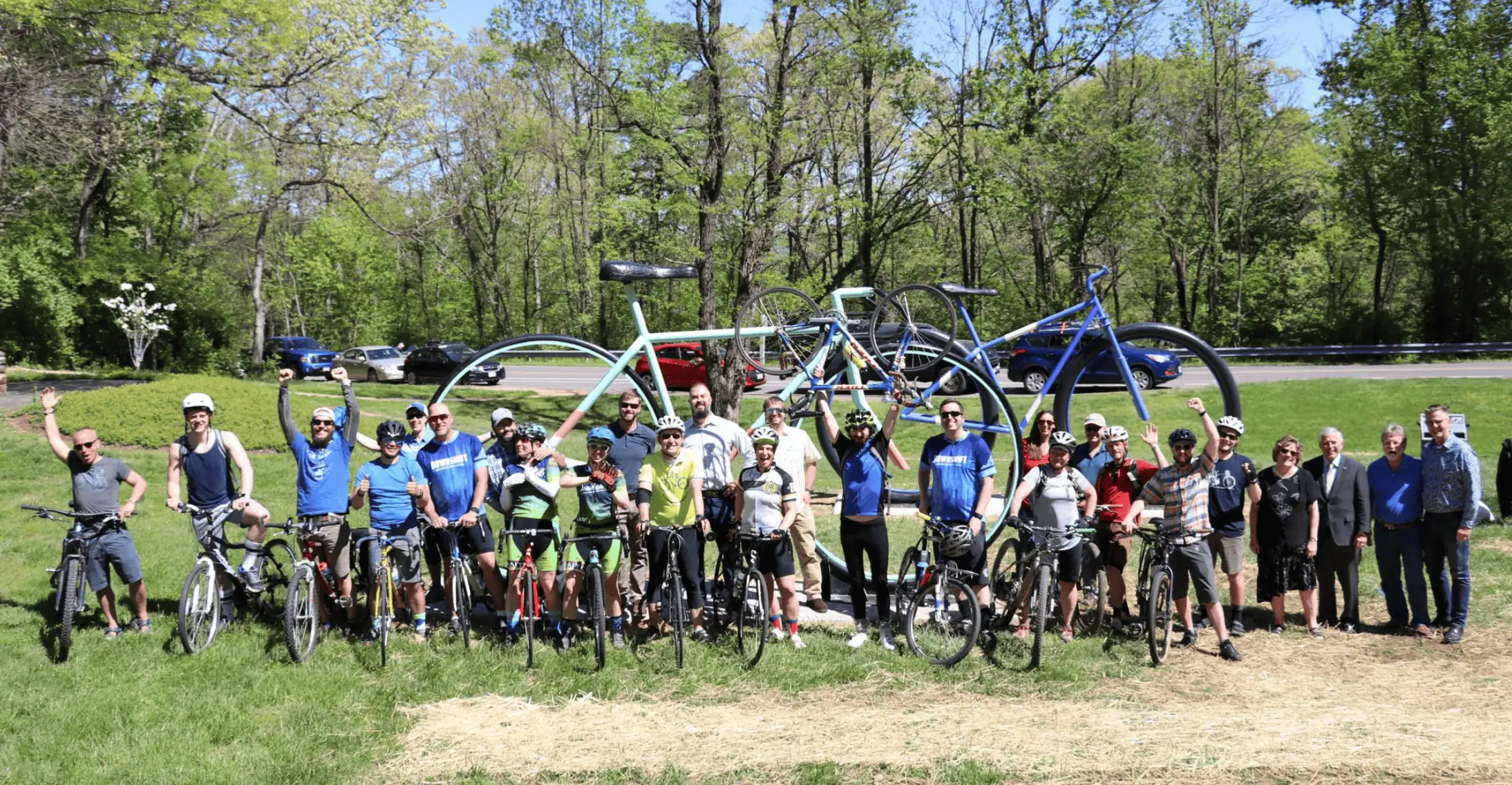 Crowd of people, some with bikes, in front of two giant bike sculptures by Jake Smith, with green park background