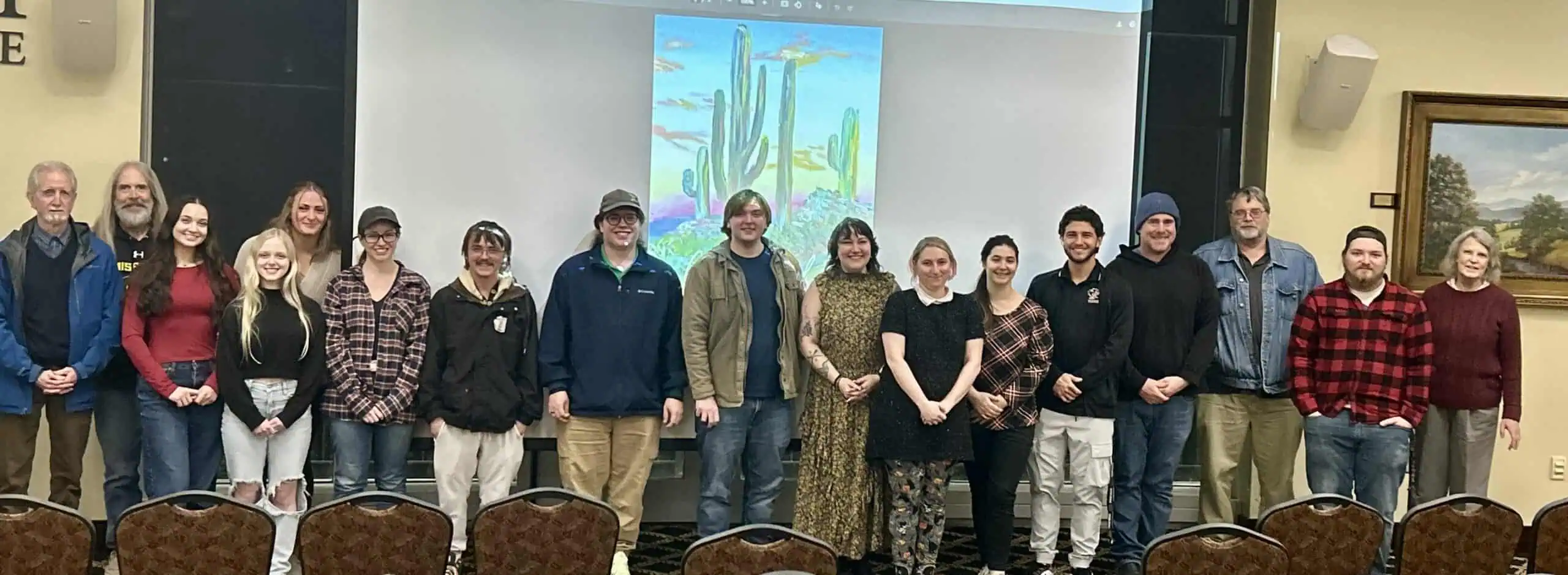 Long line of college students and faculty at Chrysalis Reveal with slide behind them showing the cover of the new issue, in bright colors with cactus on the cover, and other artworks on the told wall behind them
