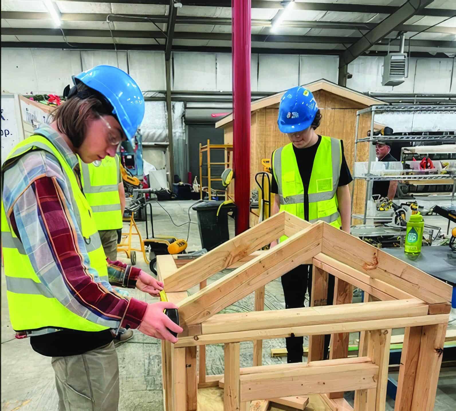 A student is measuring to ensure the project is being built correctly and to standards, while wearing his protective equipment.