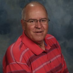 Head shot of bald man with glasses in striped shirt, shades of red/pink