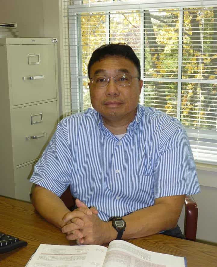 Headshot of Dr. Yili tseng in his office, in front of a window, wearing a short sleeve buttoned up blue shirt.