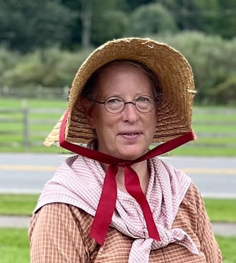 Rebecca Austin headshot in farm museum costume with straw bonnet and checked dress and kerchief.