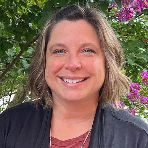 Headshot of Ferrum College staff Missy Wright standing outside in front of a floral bush.