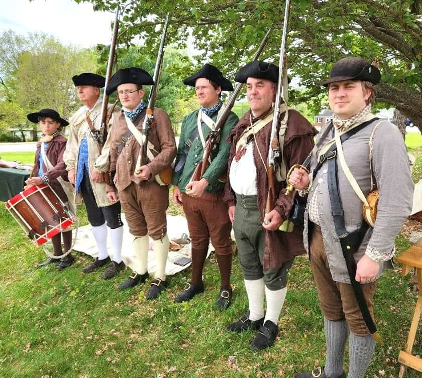 A row of men in a grassy place wearing War of Independence uniforms, several with swords, and a boy with a drum