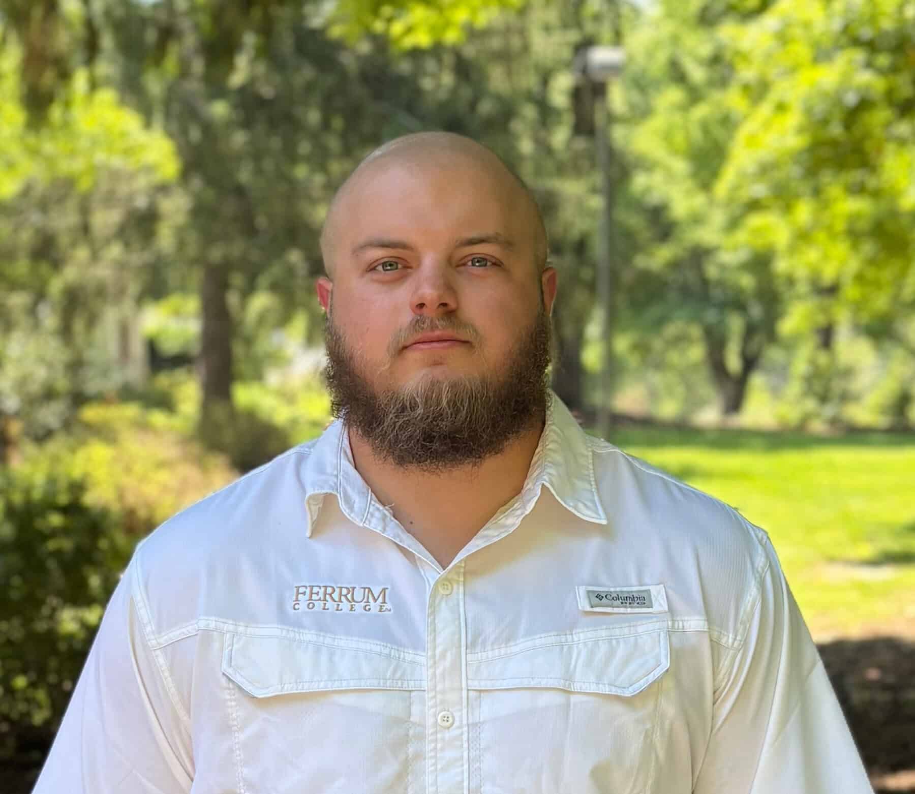 Trey Reiter standing in the shade with the trees in the background on a sunny day.