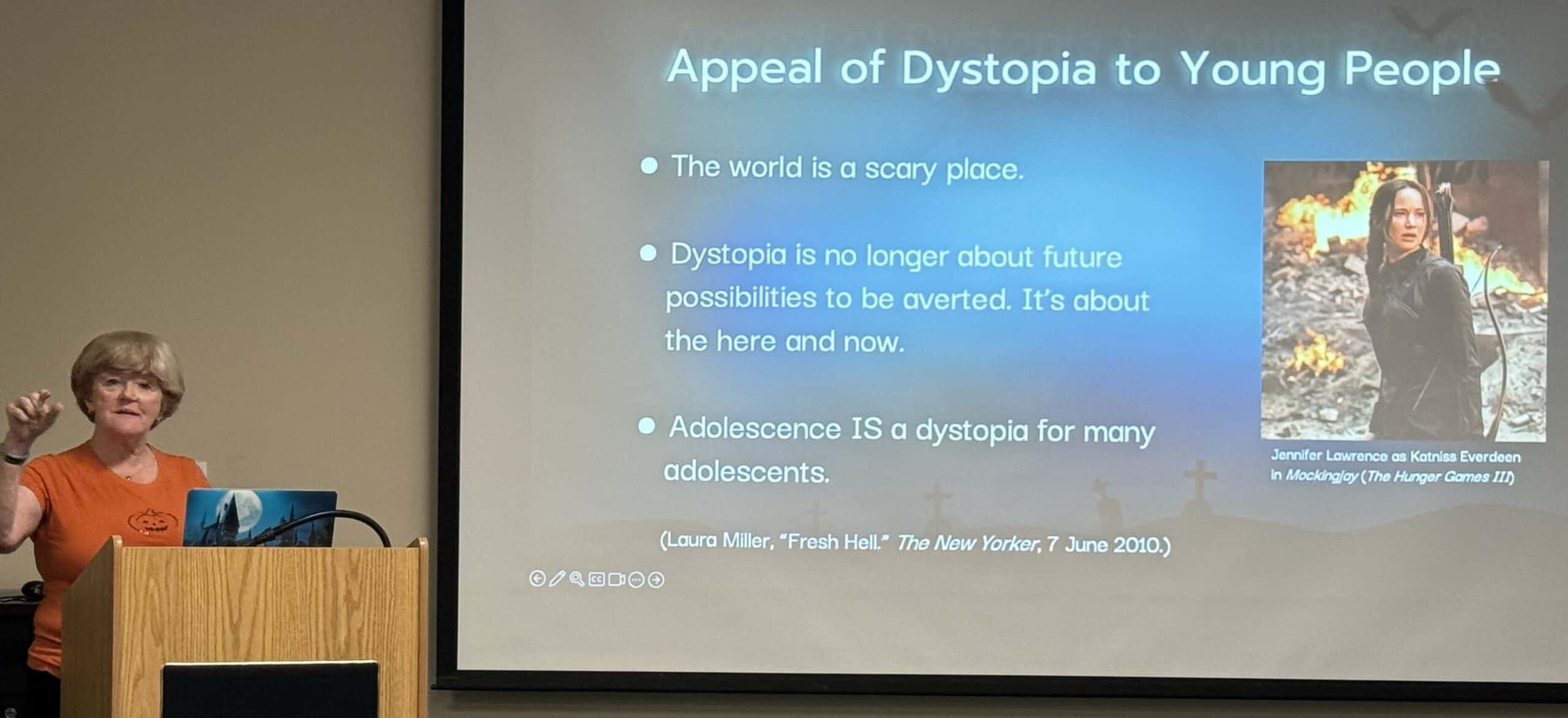 Dr. Lana Whited lecturing with slide about dystopia projected on library wall