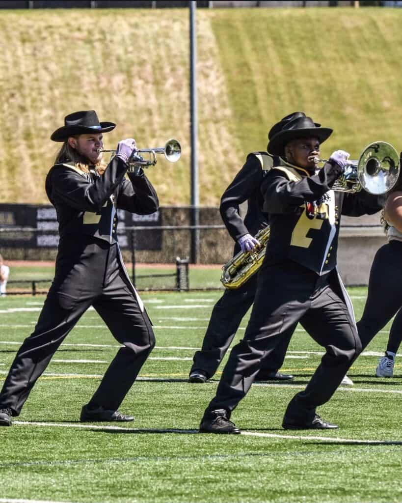 Brass instrument players wearing uniforms perform on a sports field.