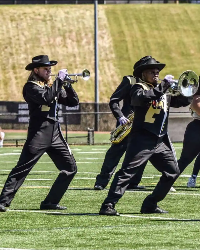 Brass instrument players wearing uniforms perform on a sports field.