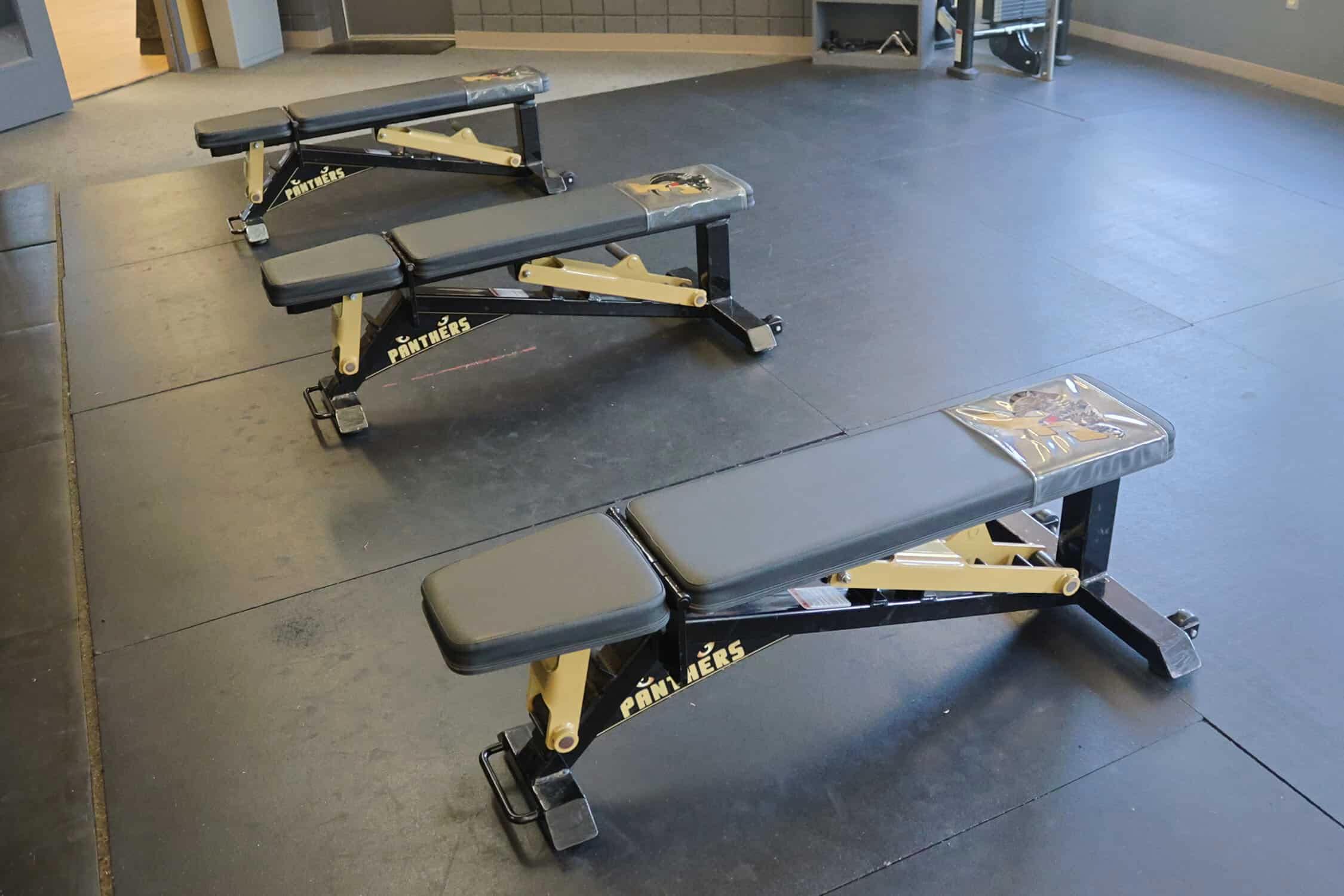 Three free weight benches at the lowest level leaving them flat. The pull down machine is behind them. The benches are resting on a rubber floor.