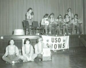 Black and white photo of young performers posing on and below a stage with a sign saying 