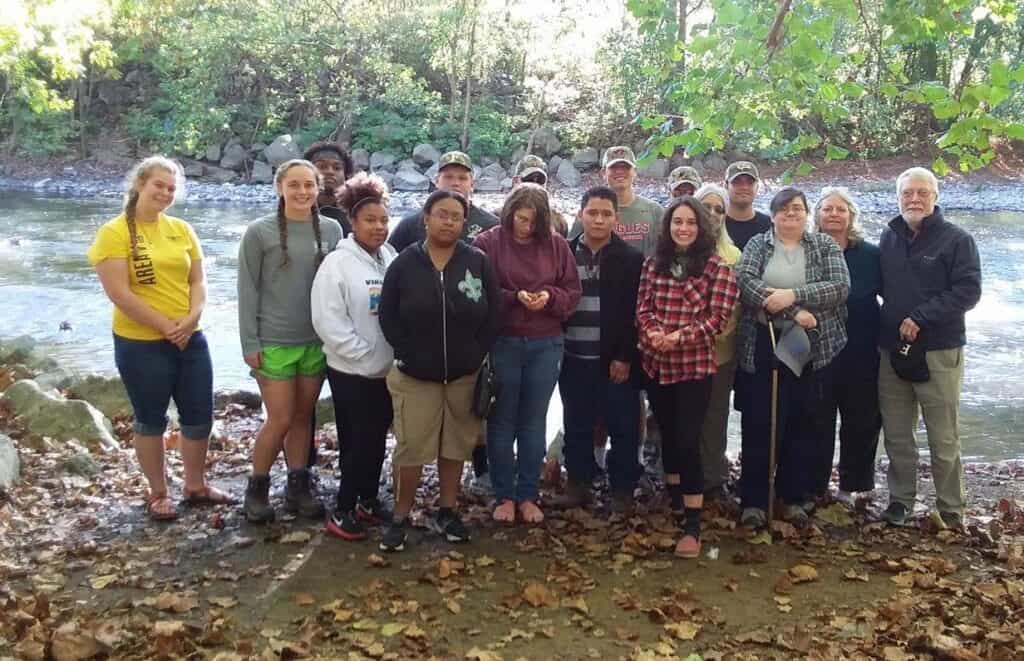 Pete Crow on right with standing group of Appalachian Cluster students and faculty by Clinch River in St. Paul, VA in 2017.