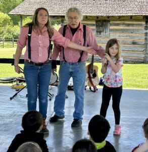 Rachel and Rex in red gingham shirts and blue child in a Jack Tale show at the farm pavilion