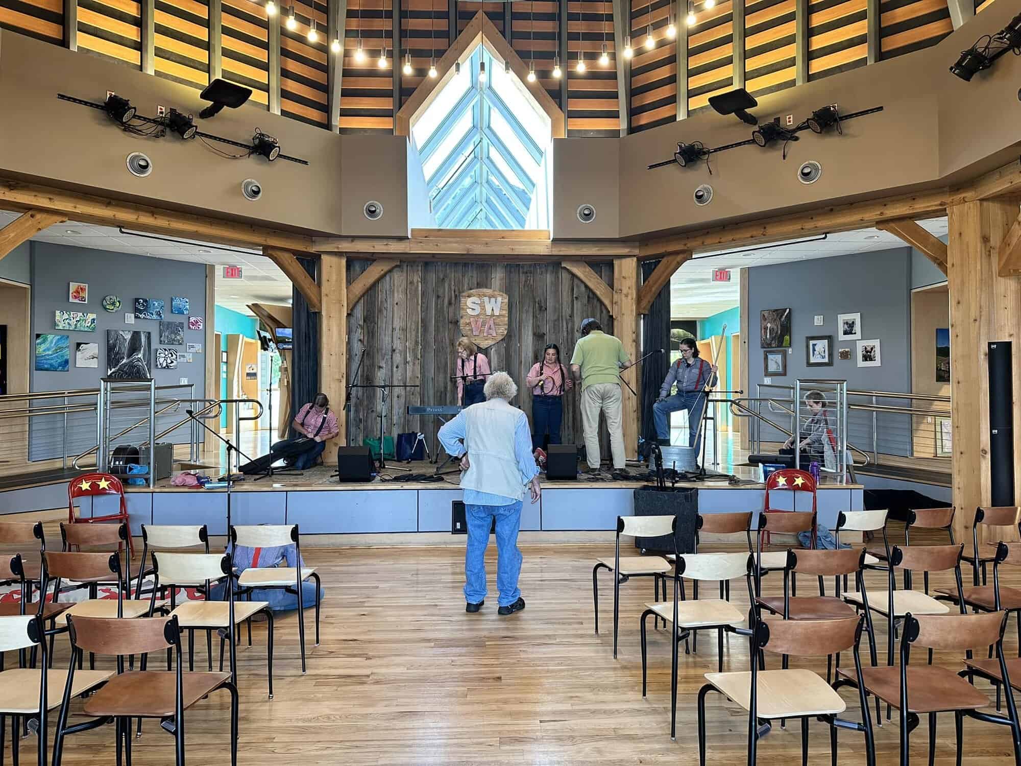 Jack Tale Players setting up on wooden stage in Abingdon with director Rex Stephenson standing on floor between chairs, wearing blue jeans and shirt, facing the stage.