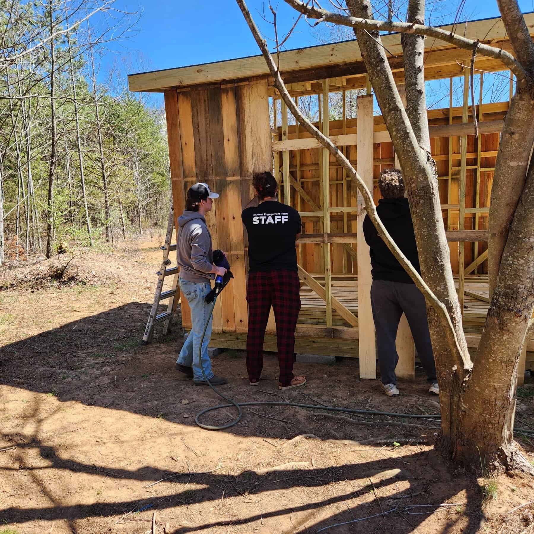 Three students helping to build a wooden shed at Ferrum Park near Ferrum College