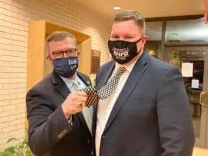 Two men stand together in dark suits, white shirts, and COVID masks over their faces. Jon Snead's mask on left says E&H. Tyler Lee's mask says RMFD.