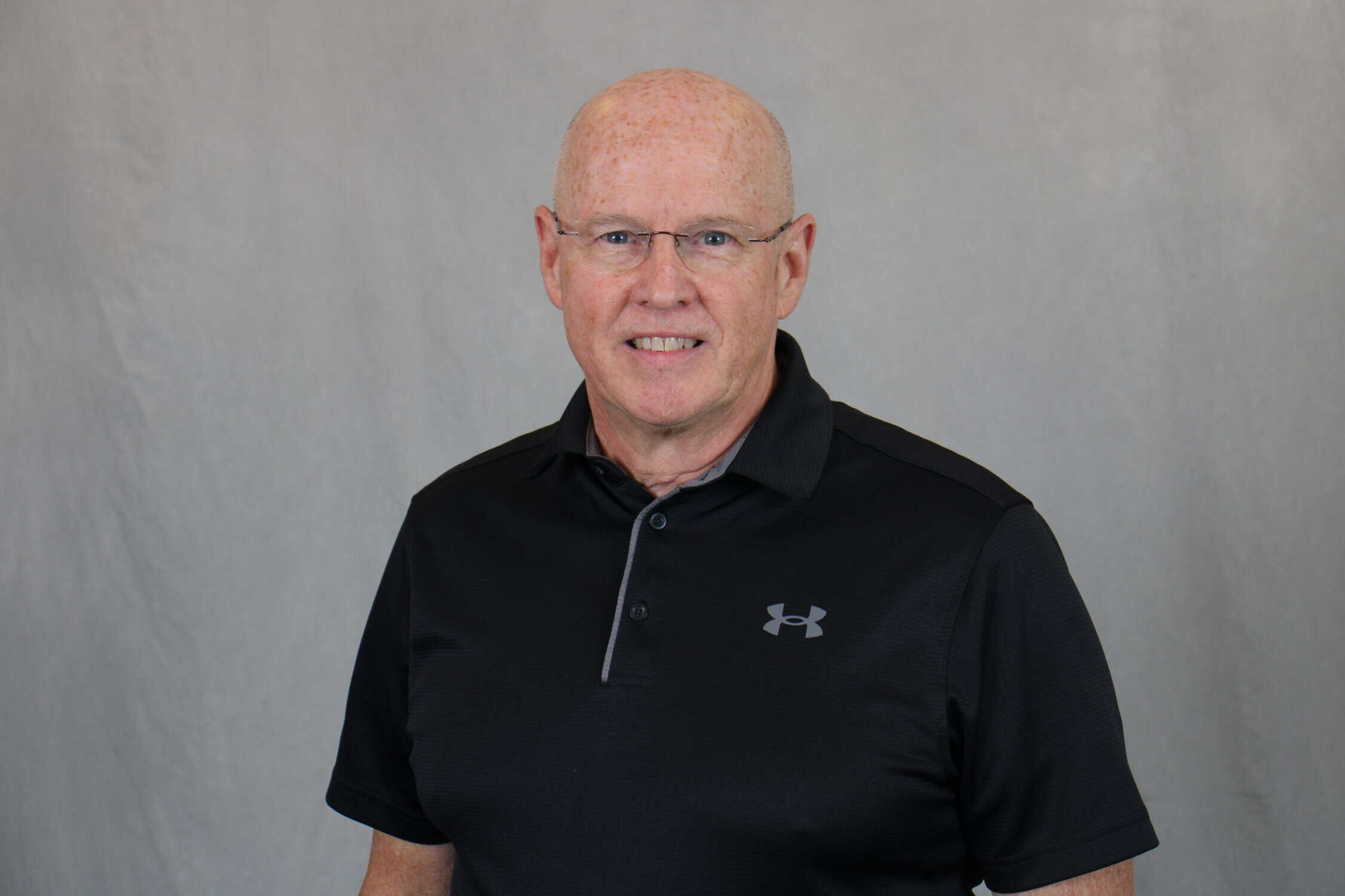 Head shot of bald man with glasses, dark shirt, and grey background