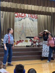 Jack Tale Players at Ferrum Elementary with Jack Tales backdrop and Tressa Moore in skirt and hat joining in