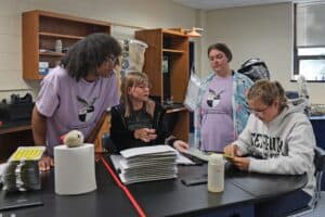 Four students working at a lab table with equipment and papers, wearing SMLA Water Quality t-shirts and Ferrum College sweatshirt