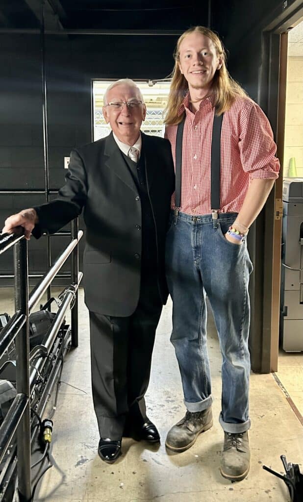 Dr. William Wray '61 in a dark suit with Jack Tale Players Django Burgess in red gingham, suspenders, and jeans