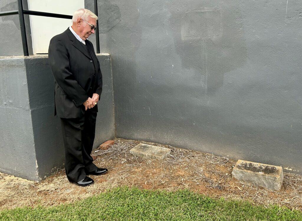 Dr. William Wray in dark suit viewing two gravestones behind Schoolfield Hall