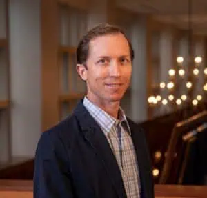 Head shot of Dr. Josh Kardos in dark suit, checked shirt, and short dark hair.