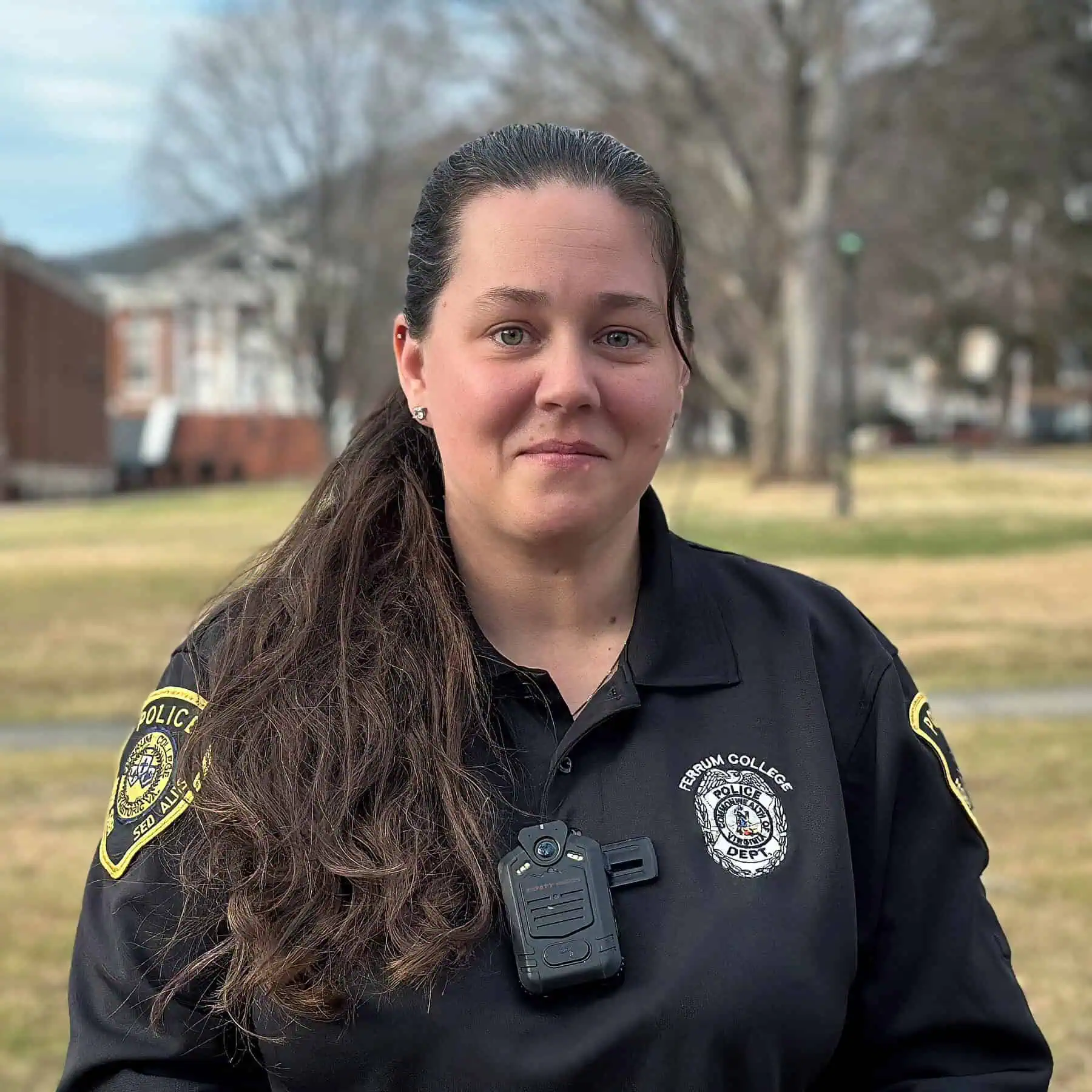 Headshot of police officer in uniform with long dark hair, in outdoor campus setting