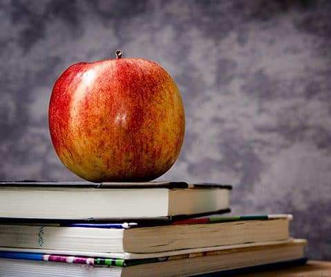 apple sitting on stack of books in front of gray marble background