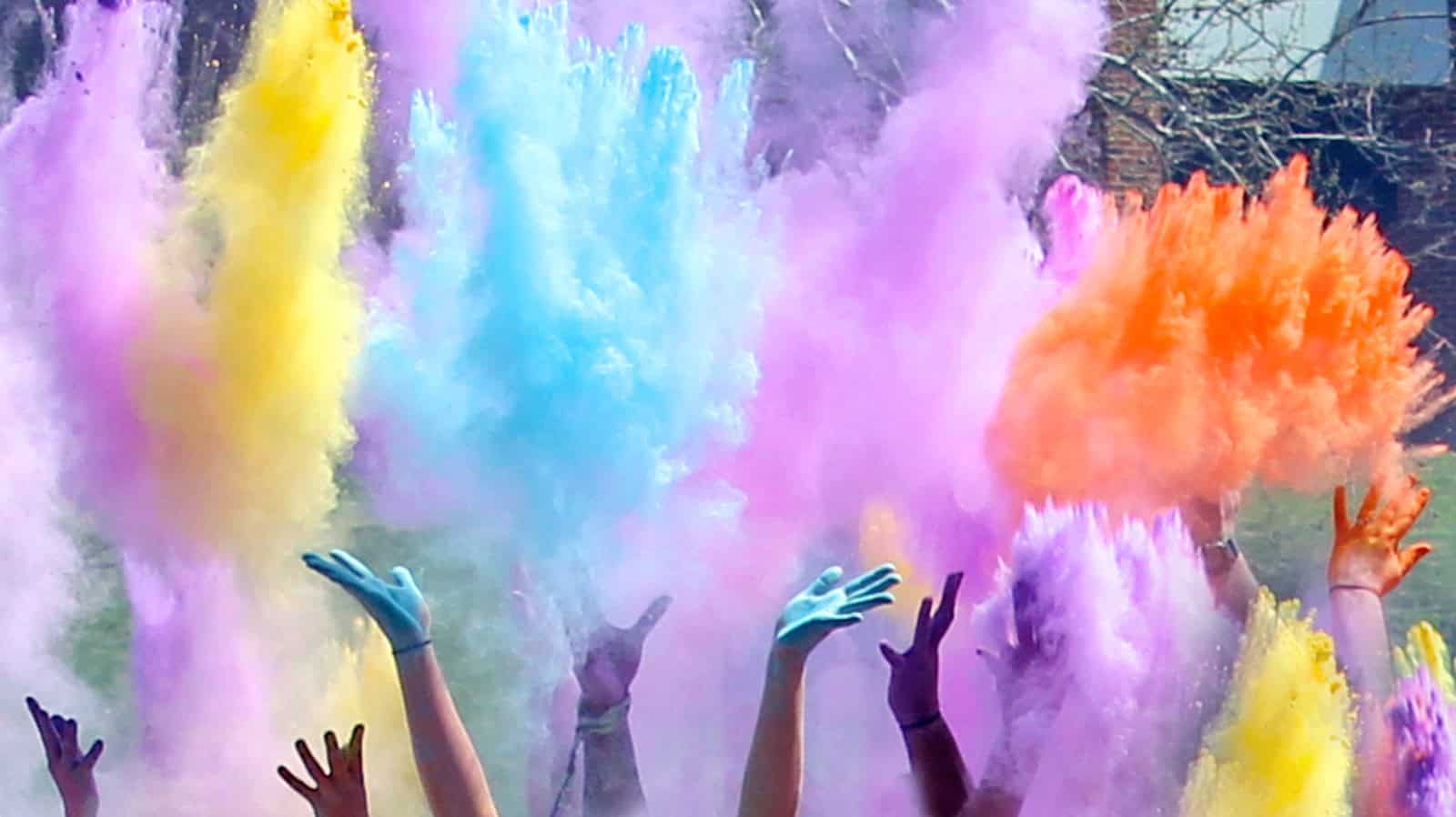 Hands are tossing a variety of colored powder in the air during a color run at Ferrum College