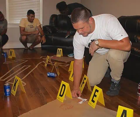 male in white shirt inspecting red shoe print at crime scene